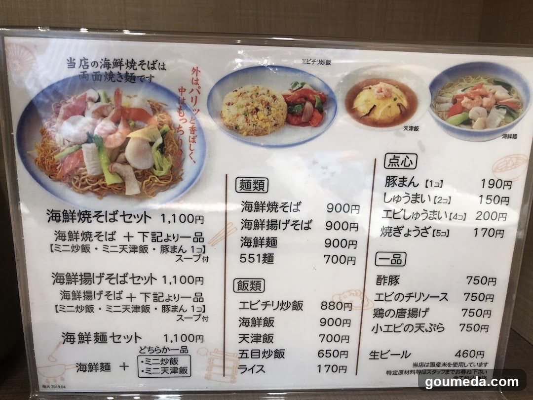 A printed menu board displaying seafood noodle dishes, rice sets, and side items with prices in yen.