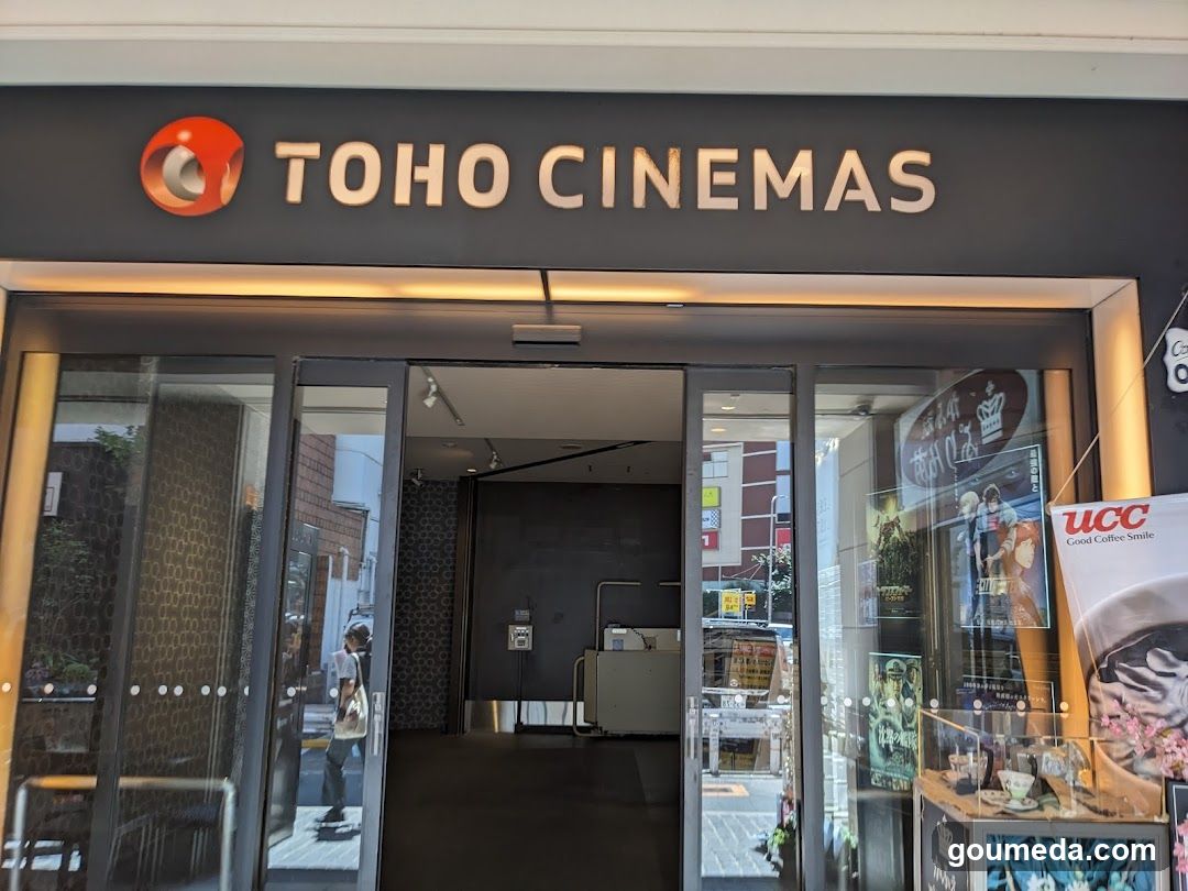 Photo of the physical exterior entrance storefront facade with visible signage reading TOHO CINEMAS above glass doors and windows displaying promotional posters.
