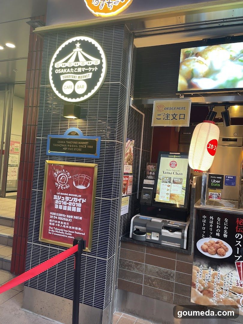 Exterior of Osaka Takoyaki Market storefront with illuminated signage, order counter, and promotional posters.
