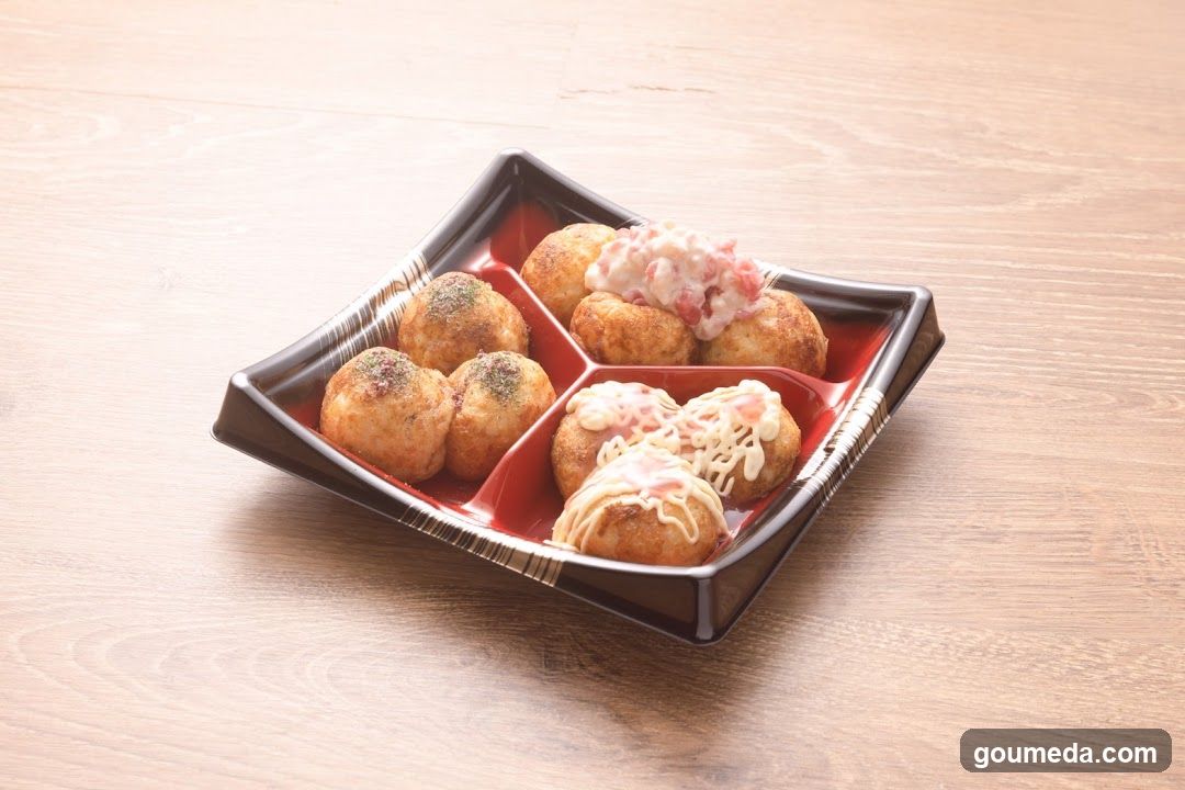 A square black tray with red compartments holds six pieces of takoyaki, Japanese street food balls made from dough and filled with octopus meat. Some are topped with mayonnaise and bonito flakes, while others have shredded cabbage or other toppings.