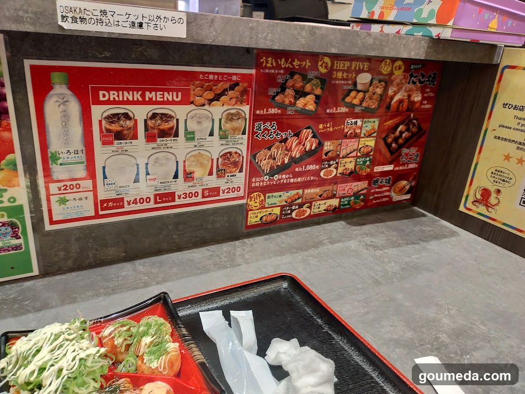 A close-up view of food items on trays, including gyoza and shredded vegetables, with a menu board displaying drink options and other food items in the background.