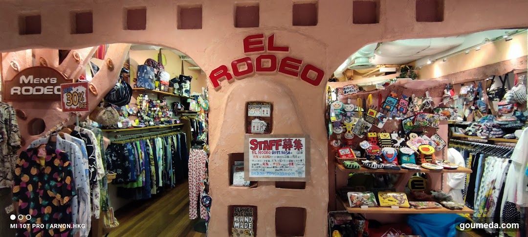 A photo of the physical exterior entrance/storefront facade with visible signage on the building. The sign reads 'EL RODEO' in red letters above an arched doorway. Inside, racks of clothing and merchandise are displayed.