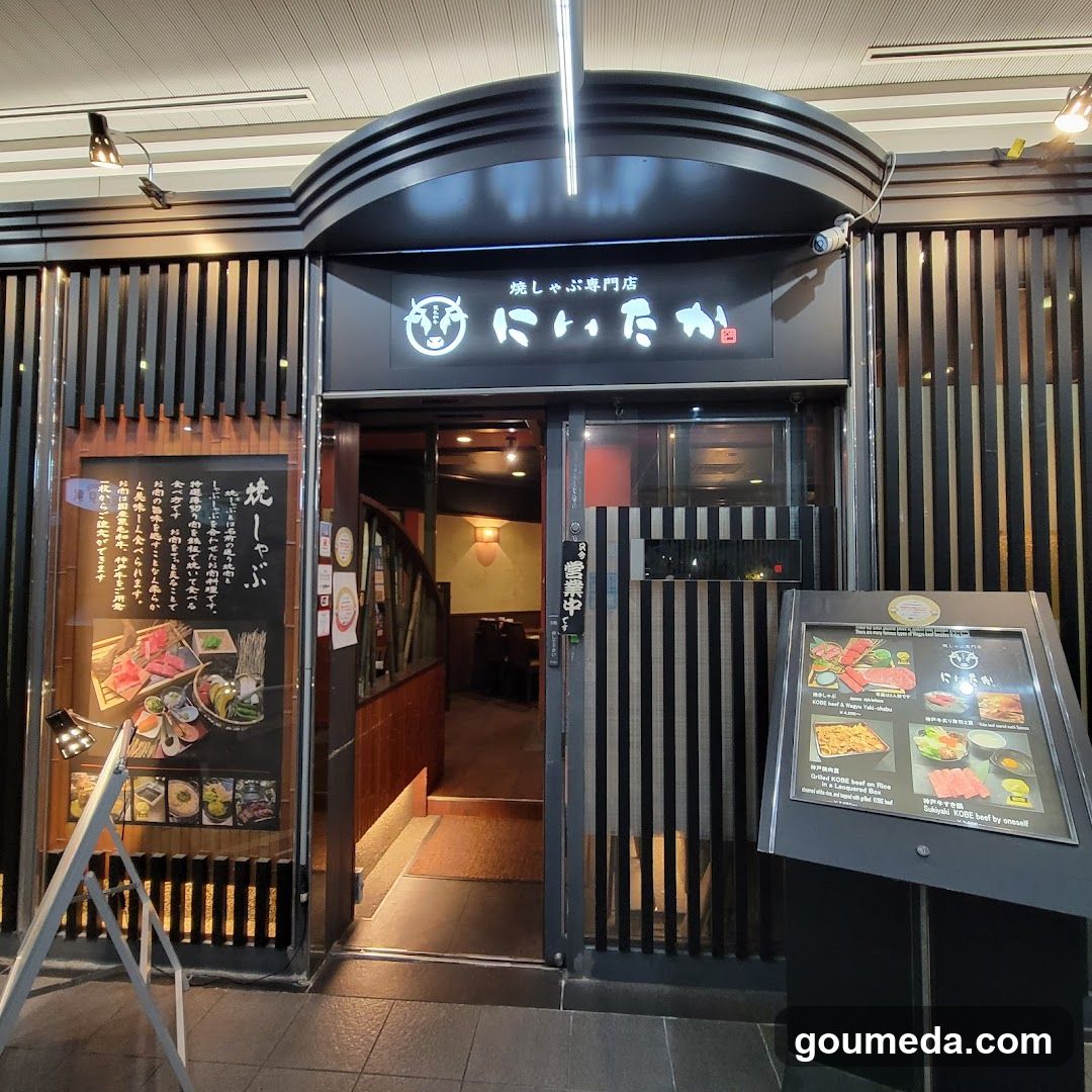 The image shows the exterior entrance of a Japanese restaurant with black and white striped wooden slats on both sides. The sign above the door reads 'にこたか' (Nikutaka) in illuminated characters, accompanied by a logo resembling a cow's head. A menu board is visible to the left, displaying various food items with descriptions and prices. To the right, there is an additional display stand showcasing more menu options.