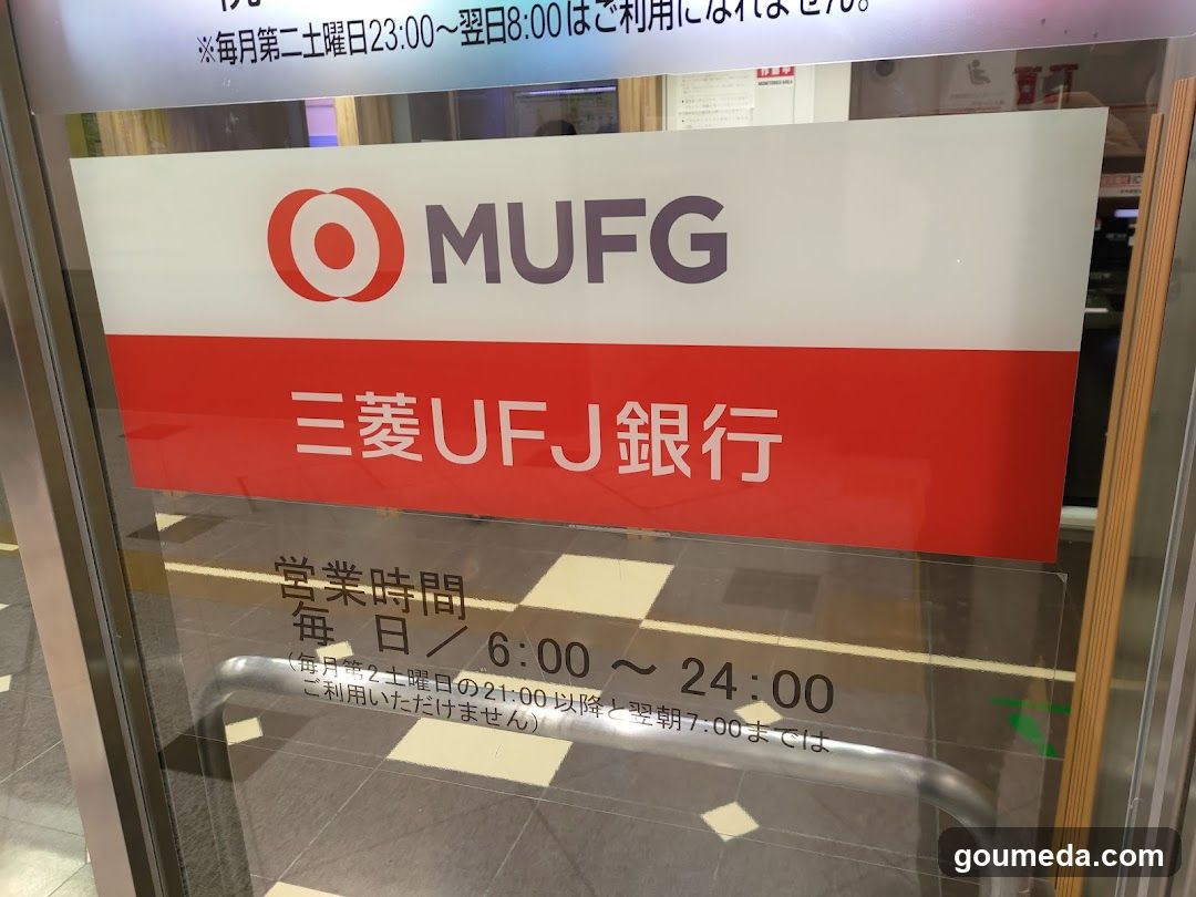 A glass door with a sign displaying the MUFG logo and Japanese text '三菱UFJ銀行'. The business hours are listed as daily from 6:00 to 24:00, with exceptions on Sundays.
