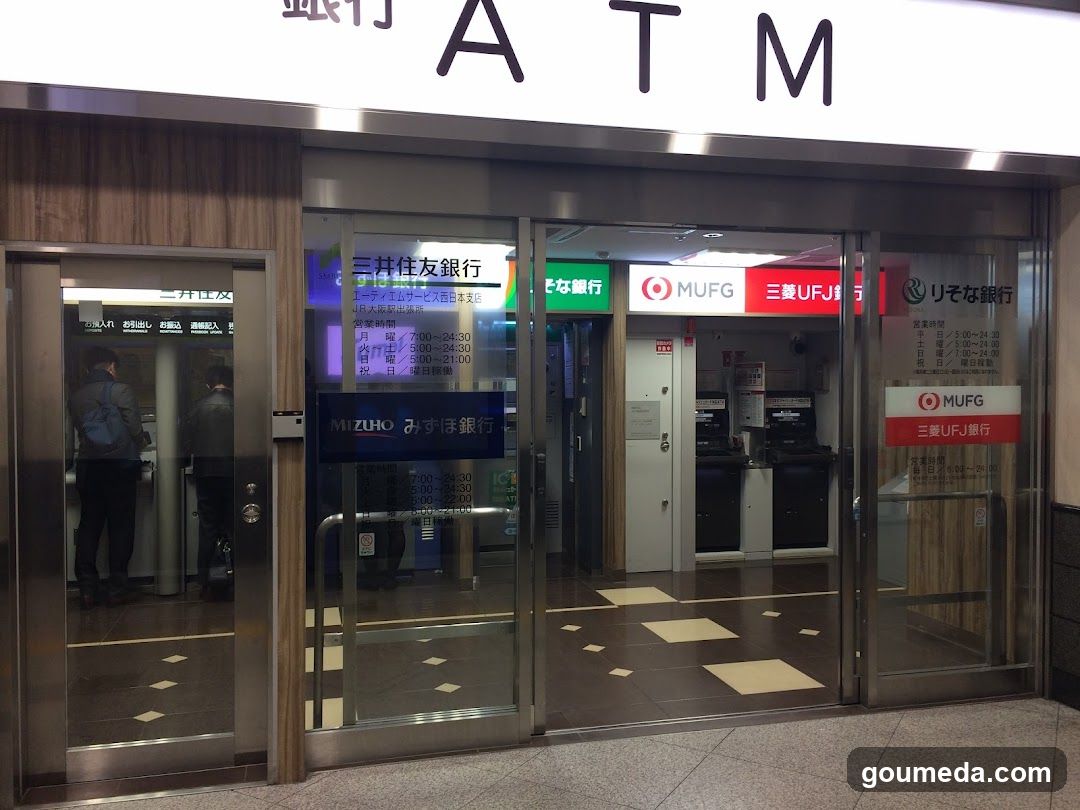 A photo of the exterior entrance to an ATM area at a bank, featuring glass doors with signage for MUFG and Mizuho banks visible on the facade.