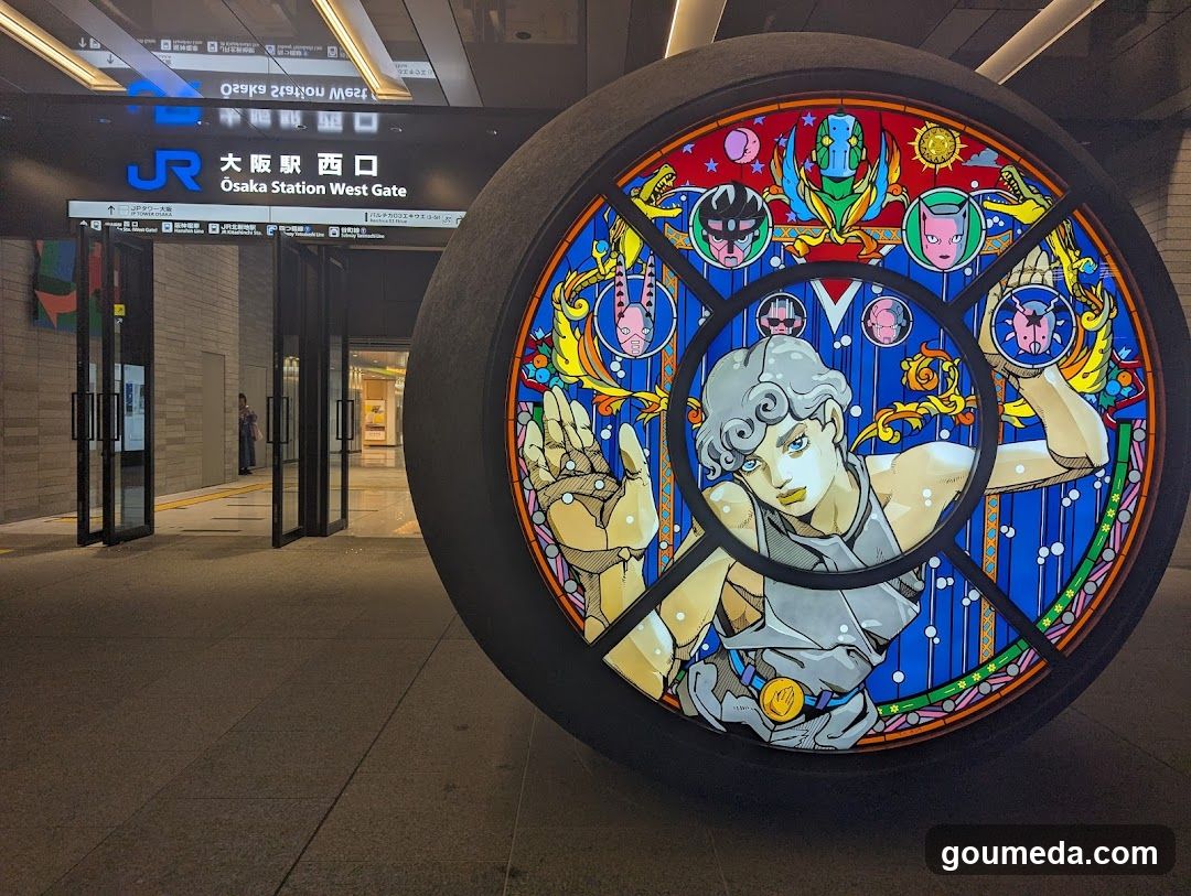 A large illuminated circular art installation featuring a character in stained-glass style dominates the foreground. In the background, the entrance to Osaka Station West Gate is visible with signage displaying 'JR' and Japanese characters alongside English text. The area appears clean and well-lit, suggesting an urban transit hub.