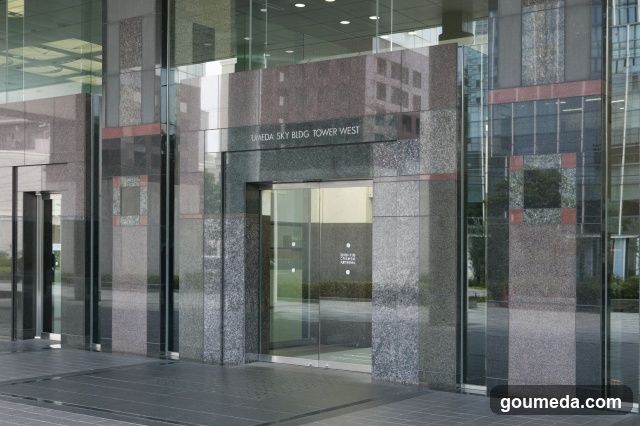 Modern glass and granite facade entrance with visible signage reading 'UMEDA SKY BLDG TOWER WEST'. No menus or printed materials present.