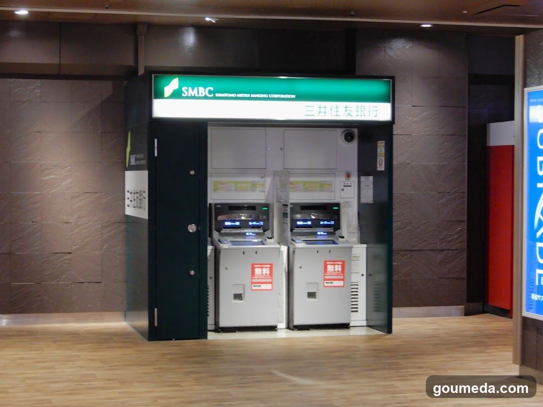 A self-service ATM kiosk with SMBC (Sumitomo Mitsui Banking Corporation) branding and signage in Japanese, located indoors on a wooden floor.