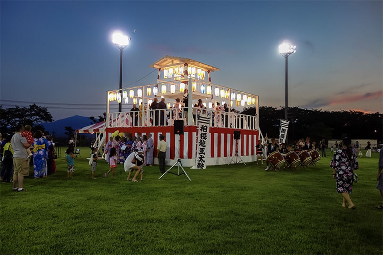 A summer festival yagura tower lit at dusk, evoking the seasonal matsuri atmosphere of the Umeda summer expo period
